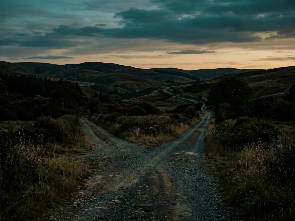 An unmarked crossroads at dusk, two empty roads running off into low hills.
