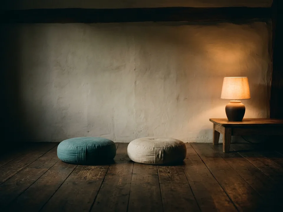 Two round meditation cushions on a bare wooden floor beside a low lamp