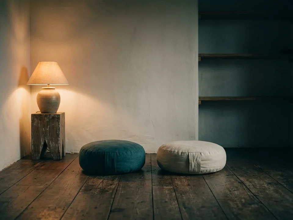 Two round meditation cushions on a bare wooden floor beside a low lamp
