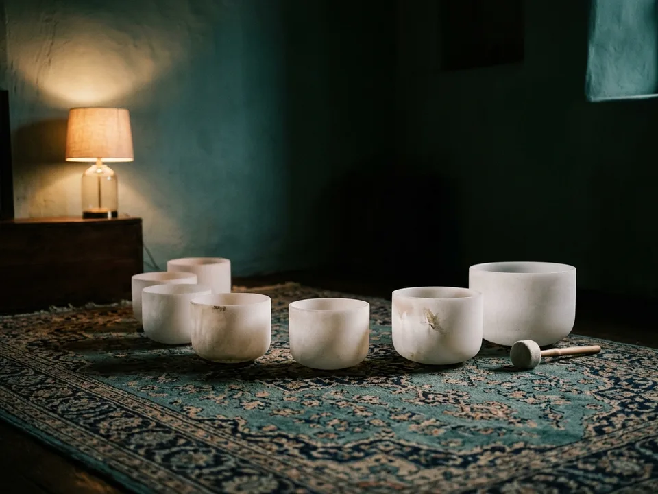 Crystal singing bowls and a mallet arranged on a rug in low lamplight
