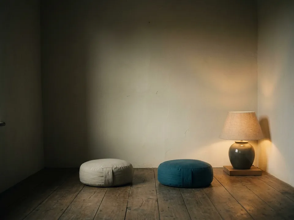 Two round meditation cushions on a bare wooden floor beside a low lamp