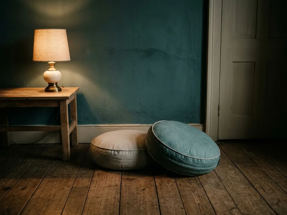 Two round meditation cushions on a bare wooden floor beside a low lamp