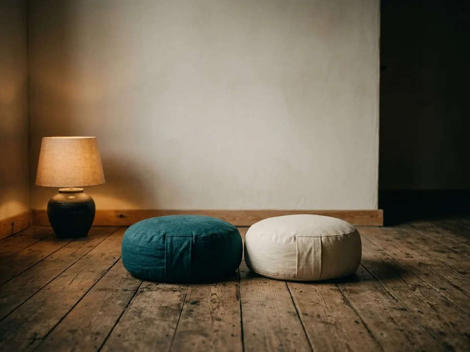 Two round meditation cushions on a bare wooden floor beside a low lamp