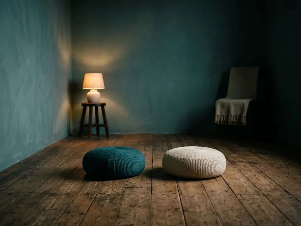 Two round meditation cushions on a bare wooden floor beside a low lamp