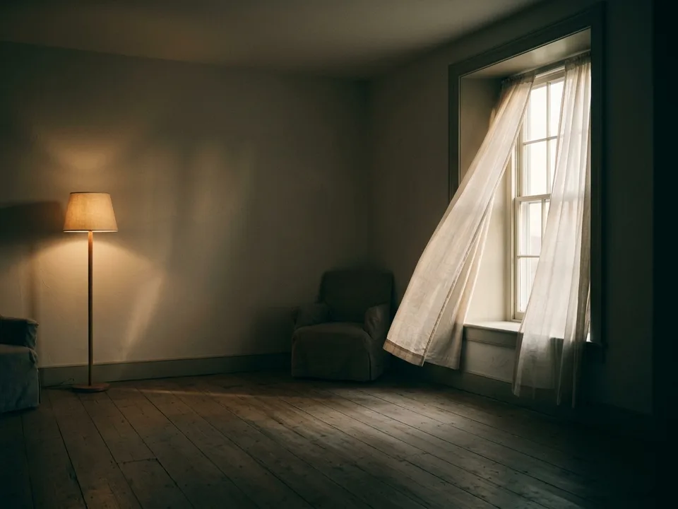 A tall window at dawn, sheer curtains and first light across an empty floor