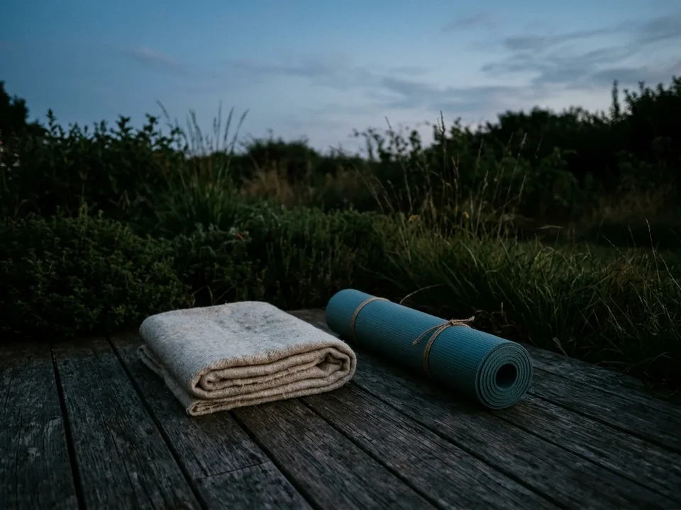 A rolled yoga mat and a folded blanket on a wooden floor in morning light