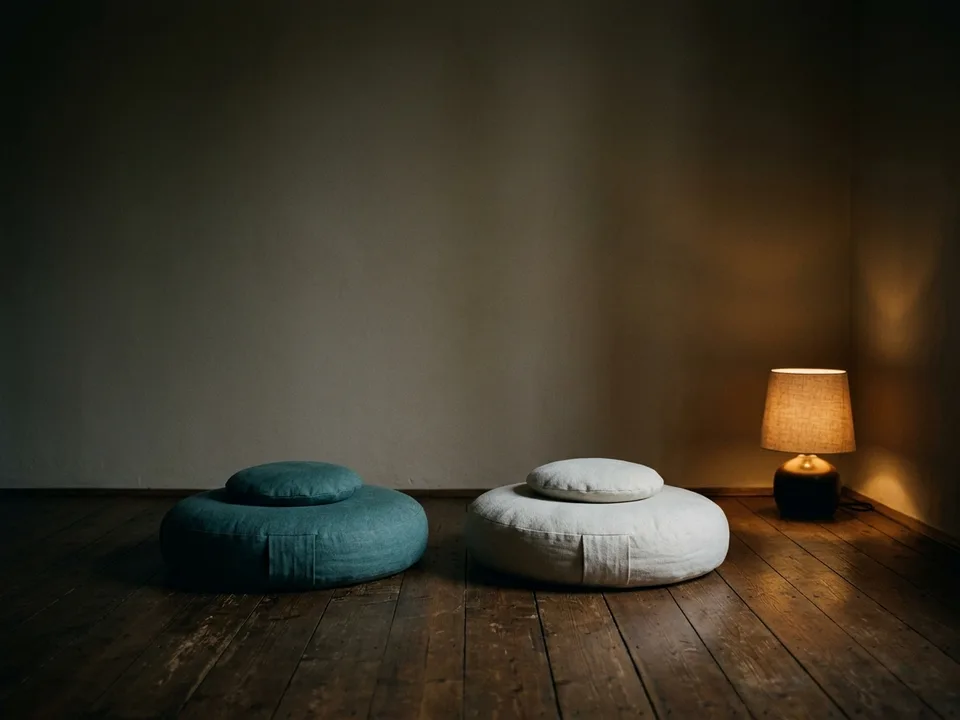 Two round meditation cushions on a bare wooden floor beside a low lamp