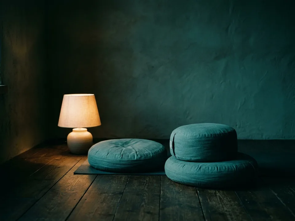 Two round meditation cushions on a bare wooden floor beside a low lamp