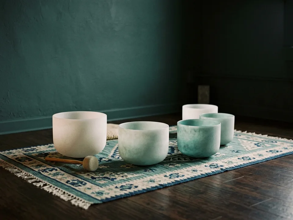 Crystal singing bowls and a mallet arranged on a rug in low lamplight