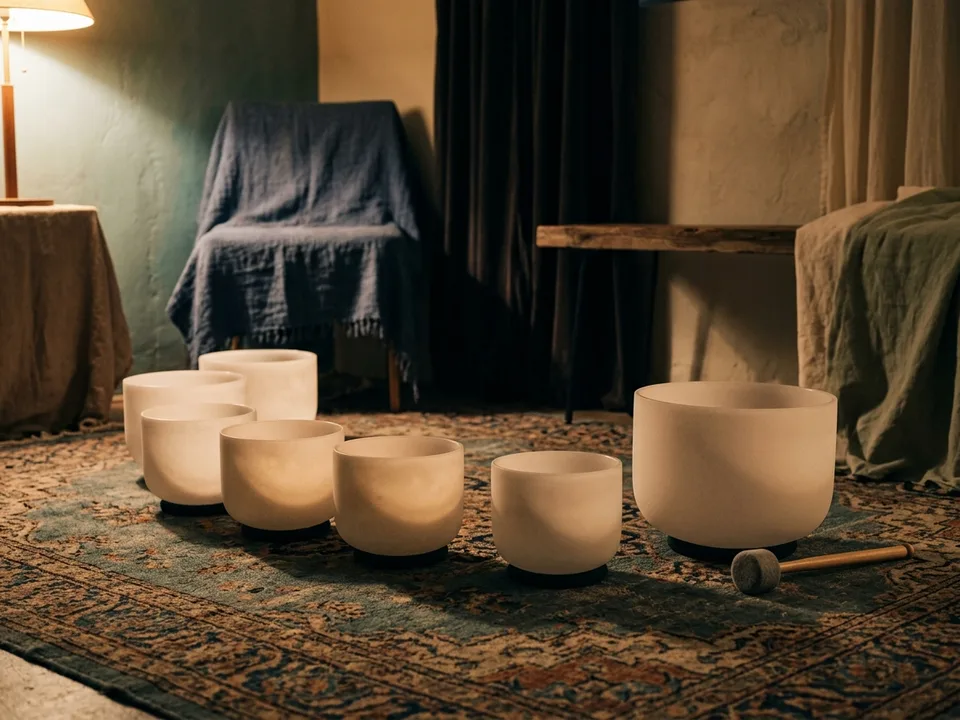 Crystal singing bowls and a mallet arranged on a rug in low lamplight
