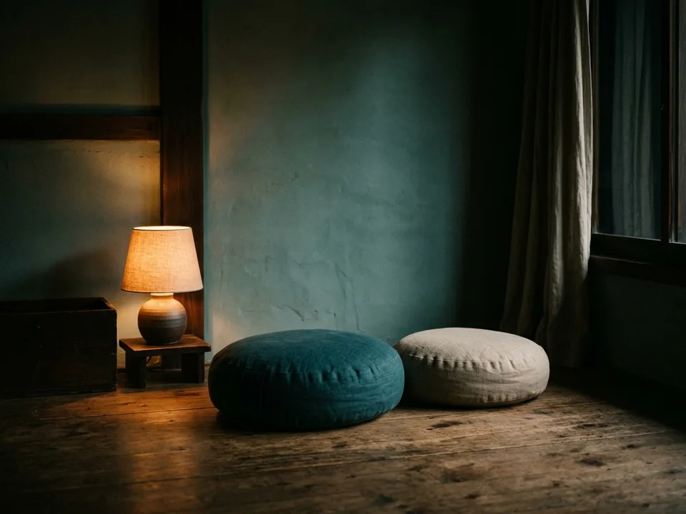 Two round meditation cushions on a bare wooden floor beside a low lamp