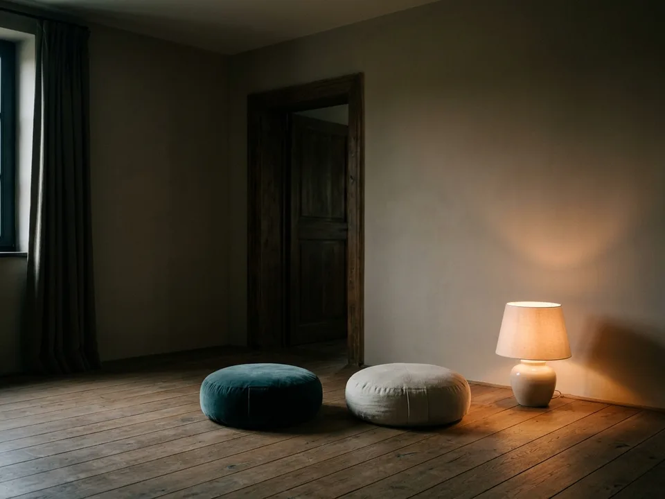 Two round meditation cushions on a bare wooden floor beside a low lamp