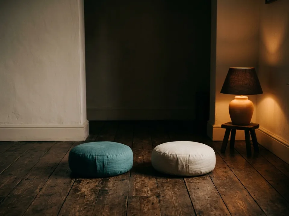 Two round meditation cushions on a bare wooden floor beside a low lamp